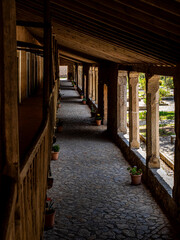 Long, shaded Porxets corridor at Lluc Monastery in Mallorca, with rustic stone columns on one side and potted plants lining the cobbled path, reflecting Mediterranean culture and historic architecture