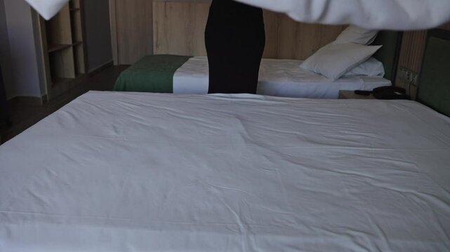 Unrecognizable woman making bed in hotel room. Maid cleaning room. Hotel room service.