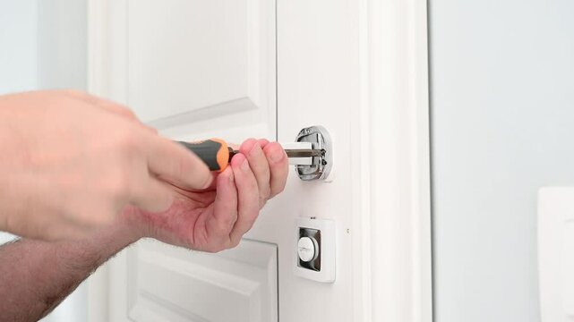 In the video, a locksmith adjusts the door handle on a modern white interior door using a screwdriver. Close-up