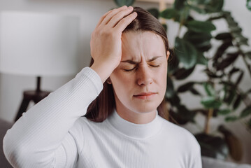 Close up of stressed young caucasian woman touching head and feels dizzy, suffering from headache...