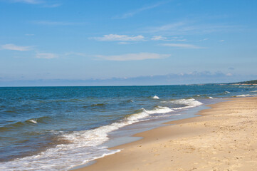 Empty, sandy beach and sea waves by sunny day