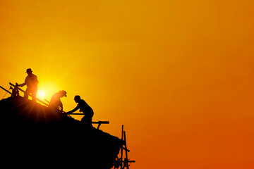 Silhouetted of Asian men construction workers working on the top of roof house without safety line around high temperature at afternoon. Background for health care or hot weather or Labor Day concept.