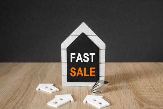 Concept words Fast Sale on black blackboard. Beautiful wooden table, black background. A stack of coins. Business concept of House Fast Sale.