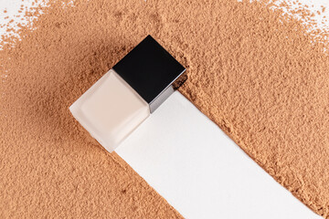 A chic bottle of liquid foundation powder lies on the trace left by the bottle on the scattered dry...