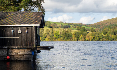 An old wooden boathouse on the lake with green landscape behind in the distance.