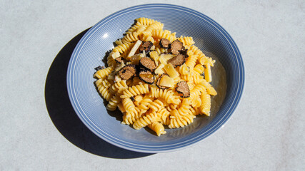 Fusilli pasta with black truffle and aged cheese, durum wheat pasta, sliced ​​fresh mushroom black truffle, parmesan cheese, luxury food, on blue plate, grey background