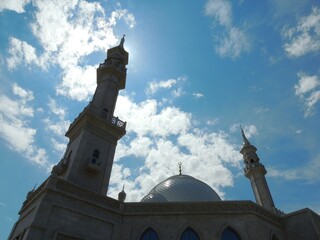 silhouette of mosque against bright blue sky with white clouds, shaded image of islamic religious...