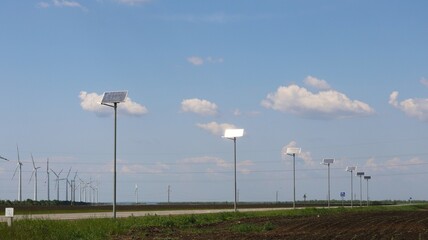 Fototapeta premium solar panels along highway with wind turbines in background, green energy of solar and wind power, renewable resources of planet earth, roadside panels and wind generators in fields