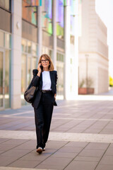 Full length of a blond haired businesswoman having a call and walking in the business district