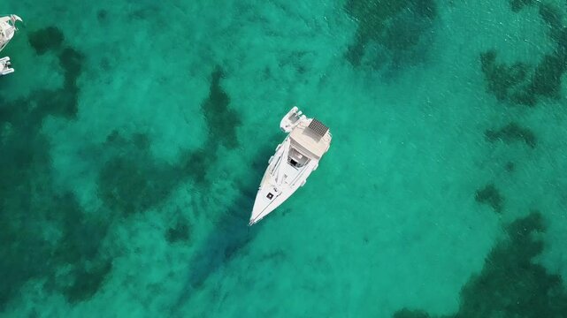 Greece,Samos Island's Posidonio Bay,Drone Footage starts from a sail boat anchored on the turquoise waters, zooms out slowly with a straight angle, at the end more boats and their shades are visible.
