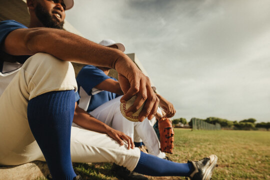 Baseball players resting on the field with a pitcher holding a baseball,