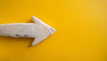 White stone arrow pointing right on yellow backdrop. Direction guide.
