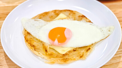 Roti Prata with Fried Egg: A close-up shot of a delicious roti prata topped with a fried egg, perfect for a breakfast or brunch menu. The roti is crispy and golden brown.