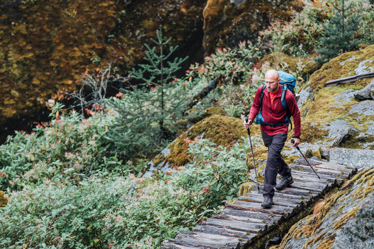 Man with backpack and trekking poles crossing mountain creek wooden bridge during Makalu Barun National Park trek in Nepal. Mountain hiking and active people concept image. - Powered by Adobe