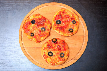 Three small pizzas with olives and cheese on wooden board