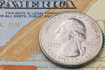 A silver quarter dollar coin sits on top of a United States of America bill