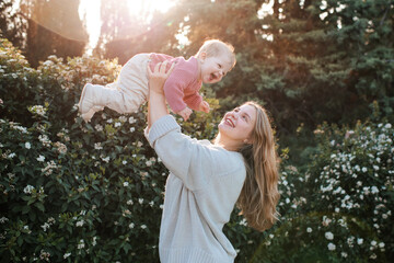 Smiling woman holding baby girl wearing knitted sweater over nature background close up....