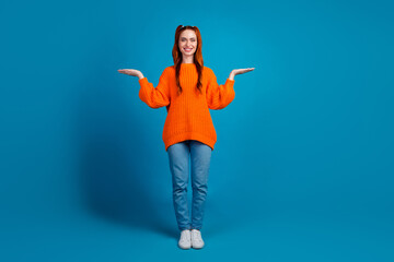 Full length photo of lovely young lady compare hold empty space dressed stylish knitwear orange garment isolated on blue color background