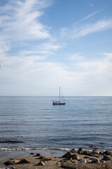A white sailboat glides across a calm ocean under a clear blue sky, representing solitude and...