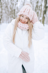 A young blonde with long hair in a white fur coat stands on the snow in the winter forest.
