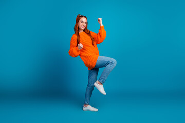 Full length photo of lovely young lady winning raise fists dressed stylish knitwear orange garment isolated on blue color background