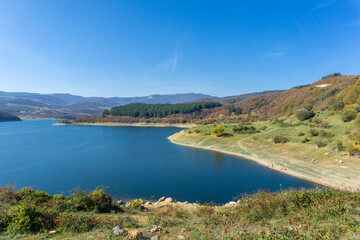 Part of the Algeti reservoir. Dark blue water surface with ripples. Low rocky banks. Forest, mountains, blue sky in the background