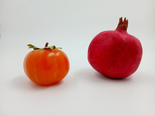 Persimmon and pomegranate isolated on a white background. Juicy fruits with vitamins. Amber and ruby colors. Sweet dessert. Plants for catalogues to the supermarket. Culinary theme or healthy eating.
