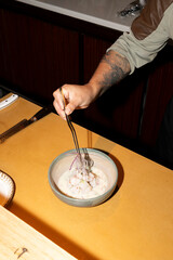 Close-up of a chef's hand delicately placing a red onion on a plate of ceviche.