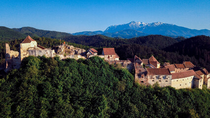 Obraz premium Rasnov Castle perched on a hilltop with snow capped mountains visible in the background