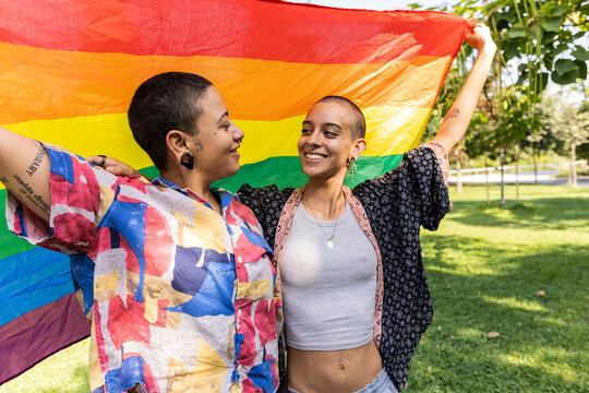 Hispanic lesbian couple celebrating with pride flag in park
