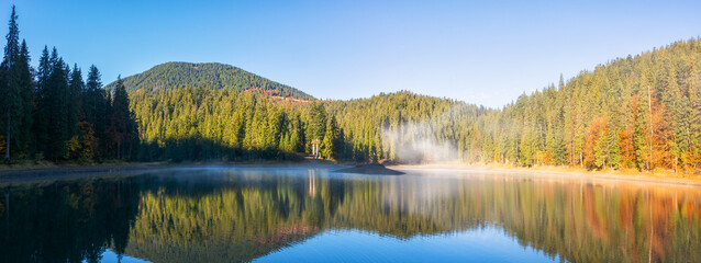 autumn landscape with lake in morning light. fog above water surface. beautiful scenery among...
