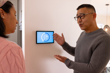 Explaining smart thermostat, asian man discussing temperature settings with wife at home