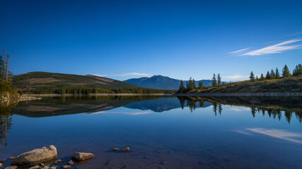 Fototapeta premium serene night scene with calm lake reflecting mountains and trees under clear blue sky. tranquil atmosphere invites peace and relaxation