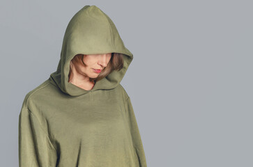 Studio portrait of sad woman in hoodie on gray background. Hood over eyes. Depression. Copy space.