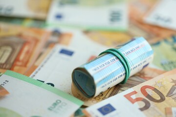 Roll of twenty euro currency bills lies on big amount of hundred and fifty euro banknotes