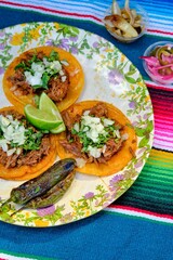 Mexican tacos with jalapenos, parsley, and fresh lime on a round plate over a colorful, striped mat