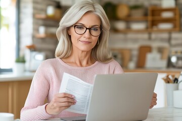 A Middle Aged Woman Wearing Glasses Holding Document, Letter or Bill Working on Laptop Sitting at Home Office Kitchen. Mature Lady Entrepreneur Looking at Camera While Checking Financial Information