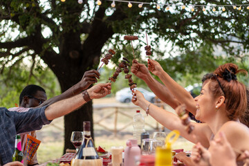 Obraz premium Friends sharing skewers at outdoor barbecue picnic with string lights, summer celebration