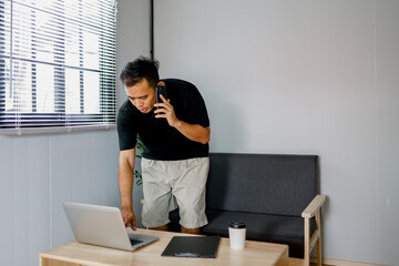 Happy young businessman talking on cell phone and using laptop

