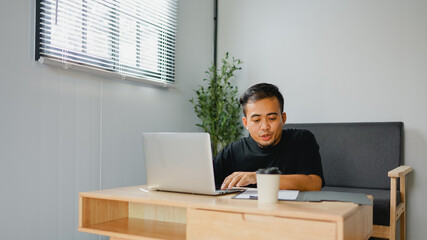 Asian businessman typing on laptop during work in cafe. Concept of remote and freelance work. Smiling adult successful man wearing. 