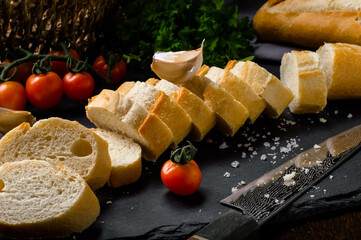 Fresh bread on black stone background. Fresh crispy french baguette on on a slate board, bakery products. Rustic bread slices with fresh tomatoes and parsley.