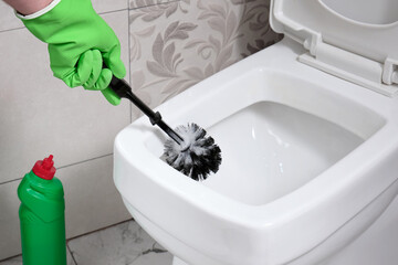 A man cleans a toilet bowl in an apartment with a brush.