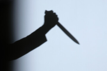 Male hand shadow holding with kitchen knife on the wall in home to night.
