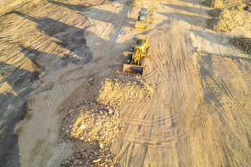 yellow tracked bulldozer performs earthworks on construction site, aerial view from a drone.