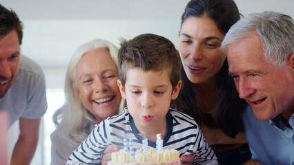 Multi Generation Family Celebrating Birthday With Grandson At Home As He Blows Out Candles