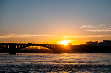 ducks swim in the Yenisei at sunset against the background of the communal bridge