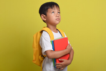 Asian boy happy holding books isolated on yellow background. Child with bright future. Back to school concept