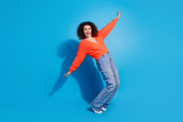 Photo portrait of wavy haired model woman wearing orange cardigan and jeans have fun flying isolated on blue color background