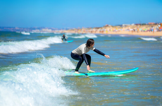Teenage girl learning to surf on foam in the ocean. First surfing lesson. Amateur surfer. Surfing training. Photo for surfing school advertising on social media.