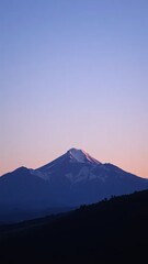 Snow-capped mountain at sunrise, with a clear sky transitioning from pink to blue, creating a serene and picturesque landscape